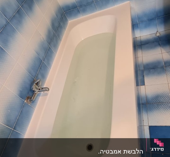 אמבטיה לבנה עם מים, אריחים כחולים על הקיר